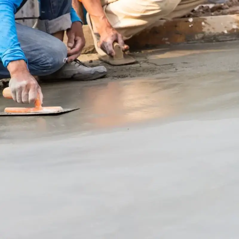 Trabajadores aplicando y alisando piso de cemento fresco con llana metálica para preparación de pulido en proyecto de Campeche