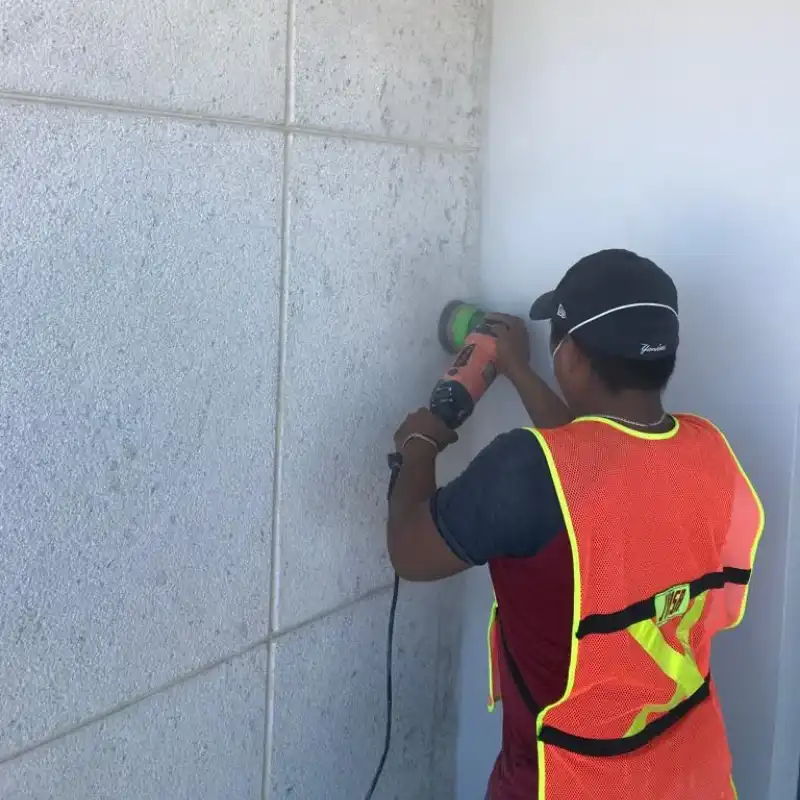 Pulido profesional de muros y fachadas de piedra en Monterrey, Nuevo León — Pulistone Técnico de Pulistone con chaleco de seguridad aplicando pulido con pulidora manual sobre muro de piedra natural en fachada de propiedad comercial en Monterrey, Nuevo León, restaurando uniformidad y acabado original